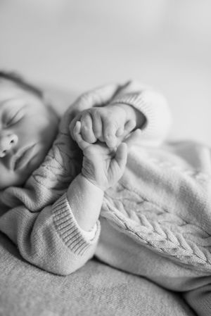 A delicate black and white photo series of tiny baby feet wearing soft knitted booties resting on textured fabric.