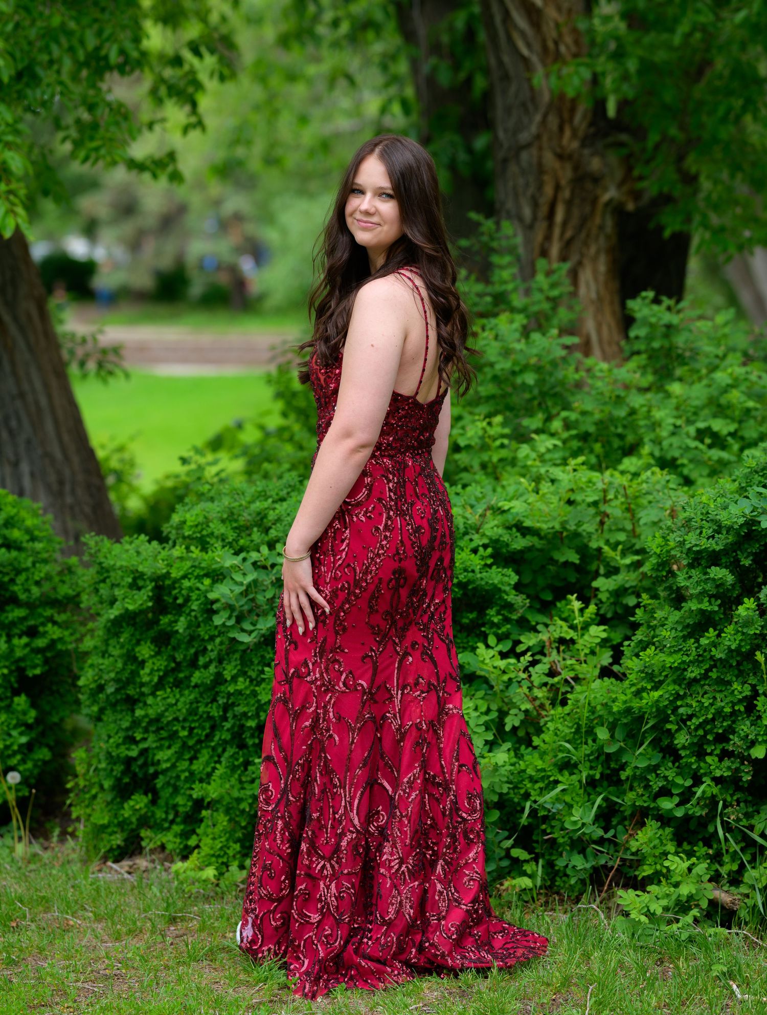 An elegant full-length view of a red sequined dress with a slit against a natural garden backdrop.
