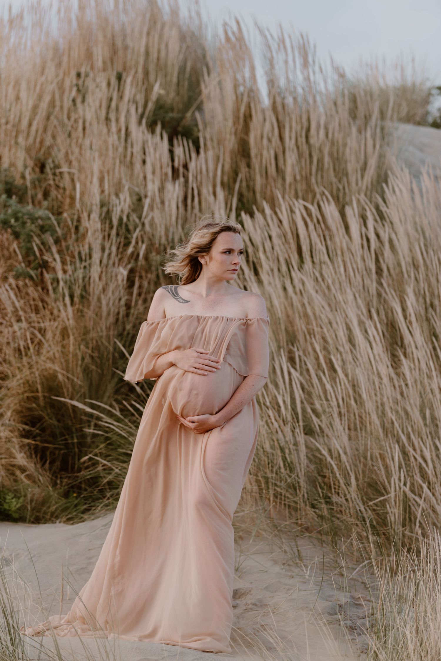 Maternity portrait in peach dress against tall pampas grass during golden hour.
