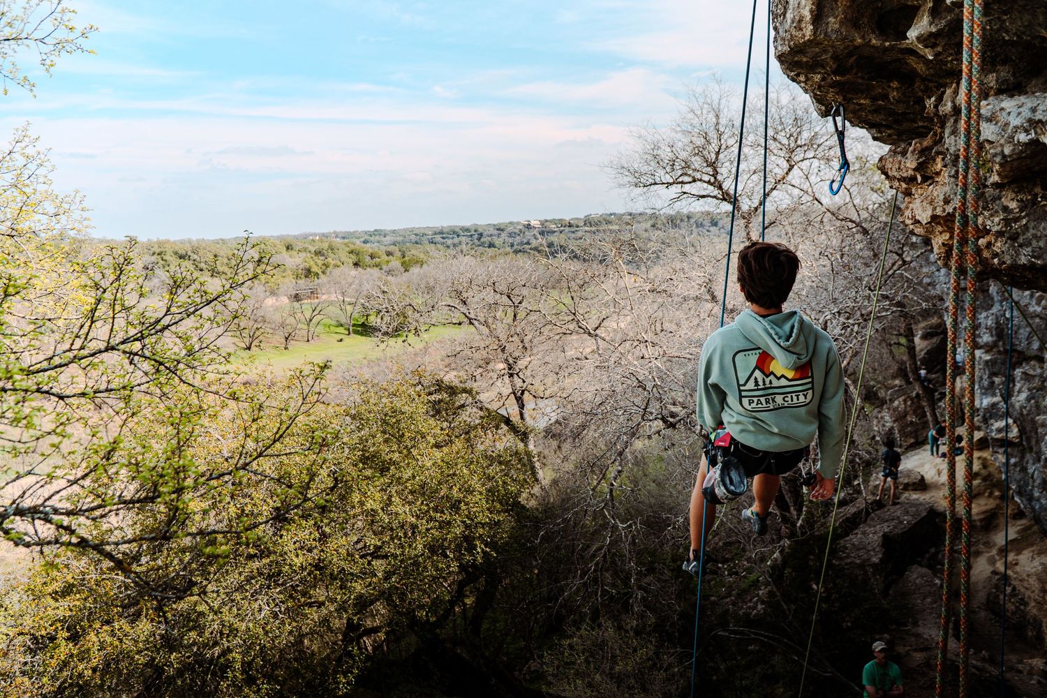 A rock climber rappels down a cliff face overlooking a scenic valley landscape.