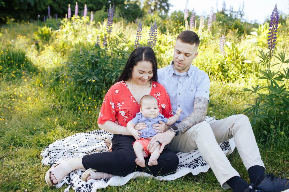 Seattle family photographer: A mother and father sit on a blanket holding their son. Lupine wildflowers can be seen in the background