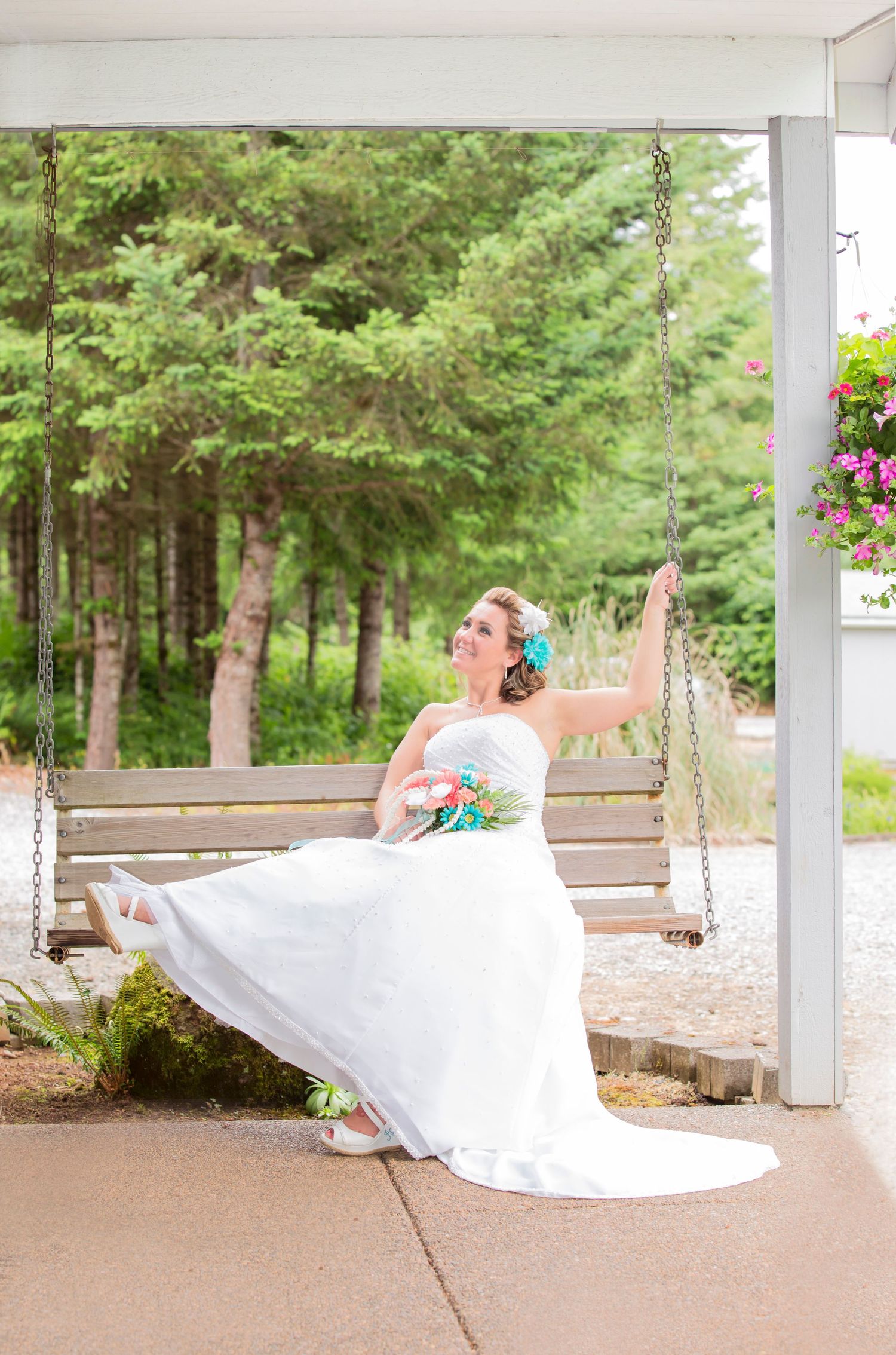 Bride in white dress sitting on porch swing with forest background.