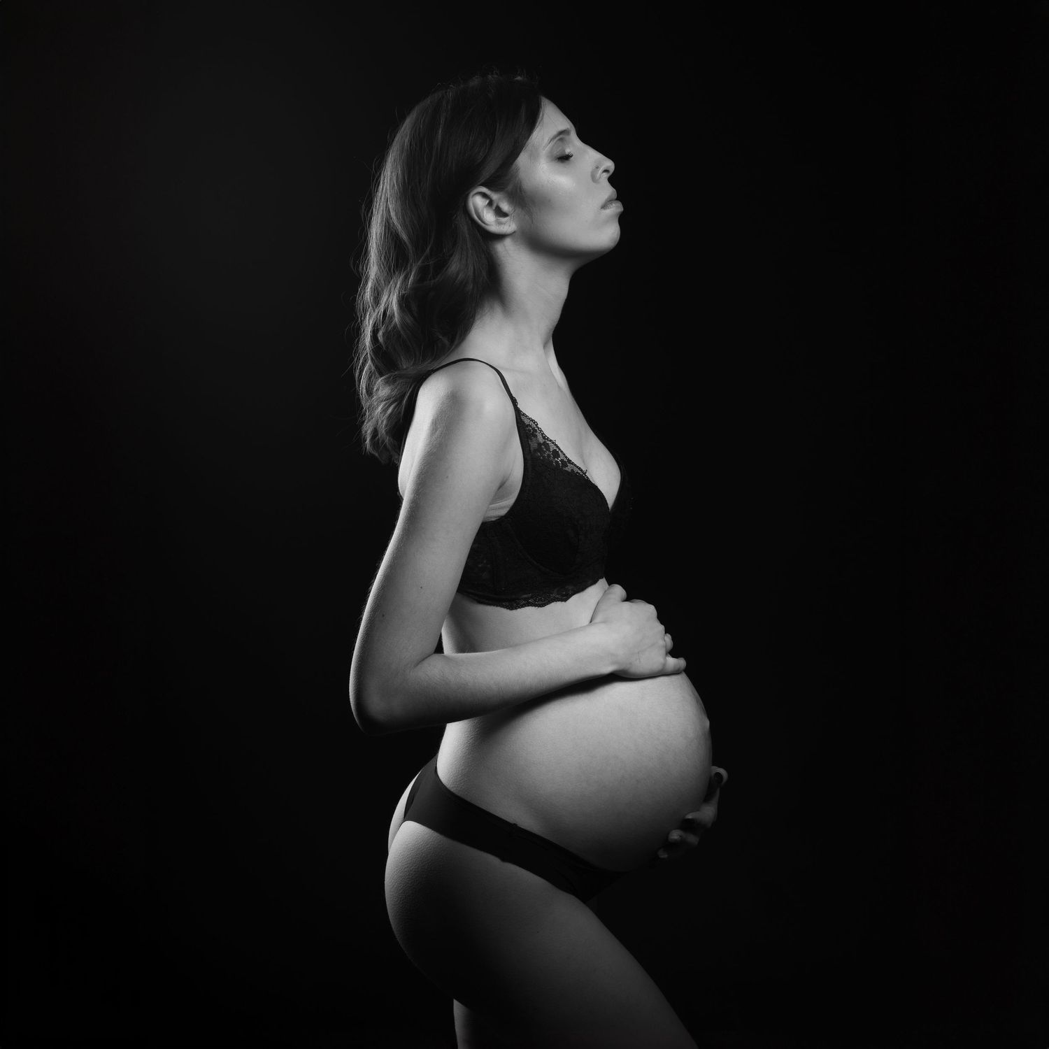 Artistic black and white maternity photo showing an expectant mother in profile against dark background.