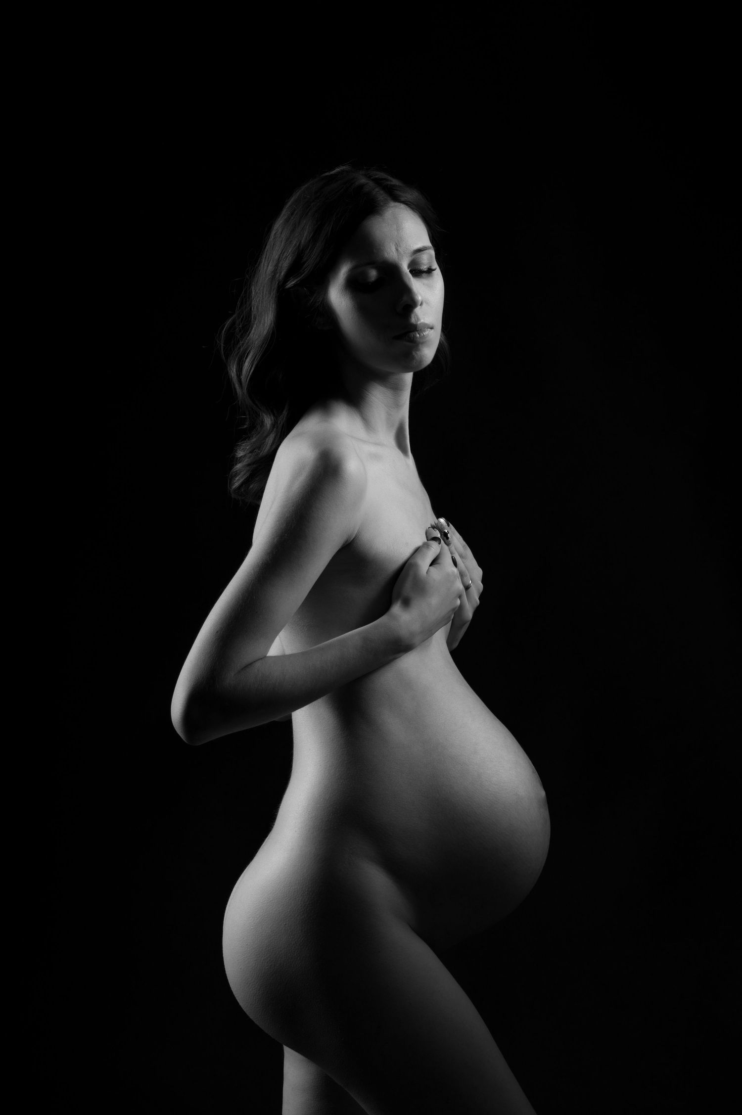 Artistic black and white maternity photo showing an expectant mother in profile against dark background.