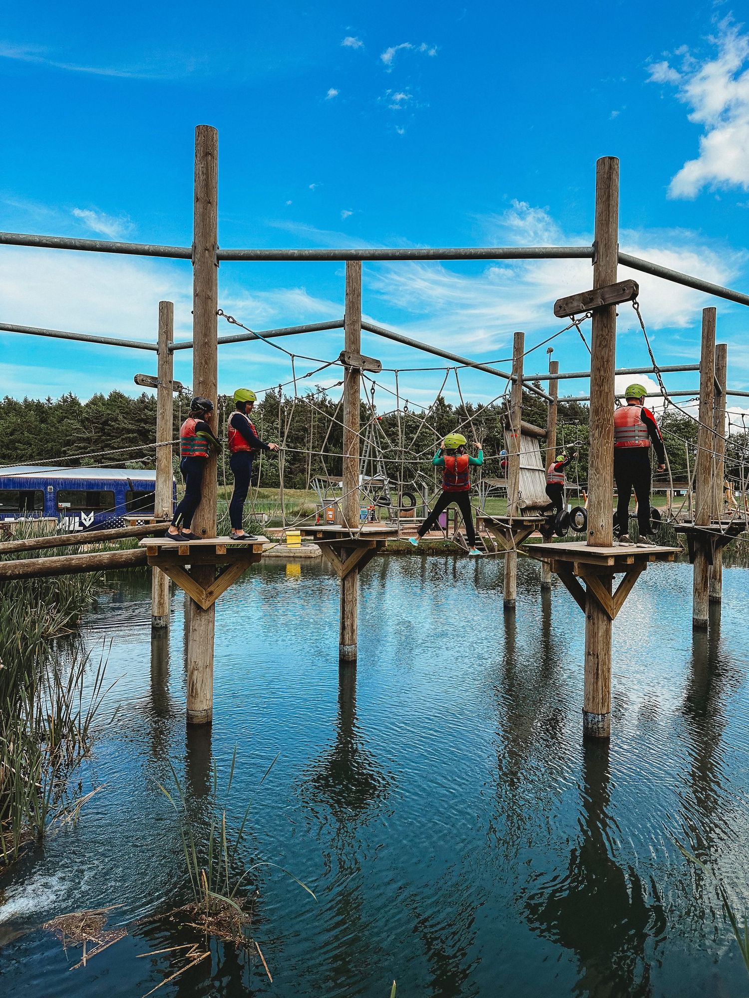 Adventure seekers crossing a wooden bridge structure over a scenic pond.
