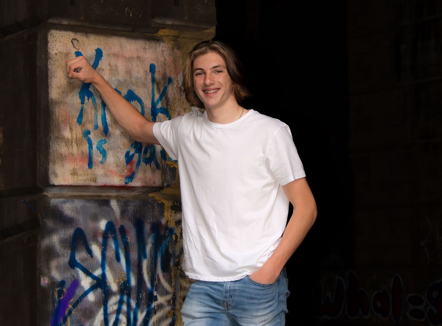 Person in casual attire poses against urban brick wall with graffiti artwork.