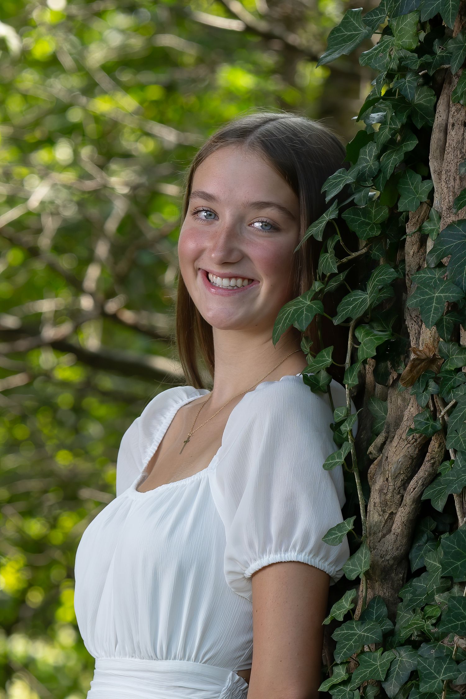Portrait session in white dress among ivy-covered trees with natural lighting.