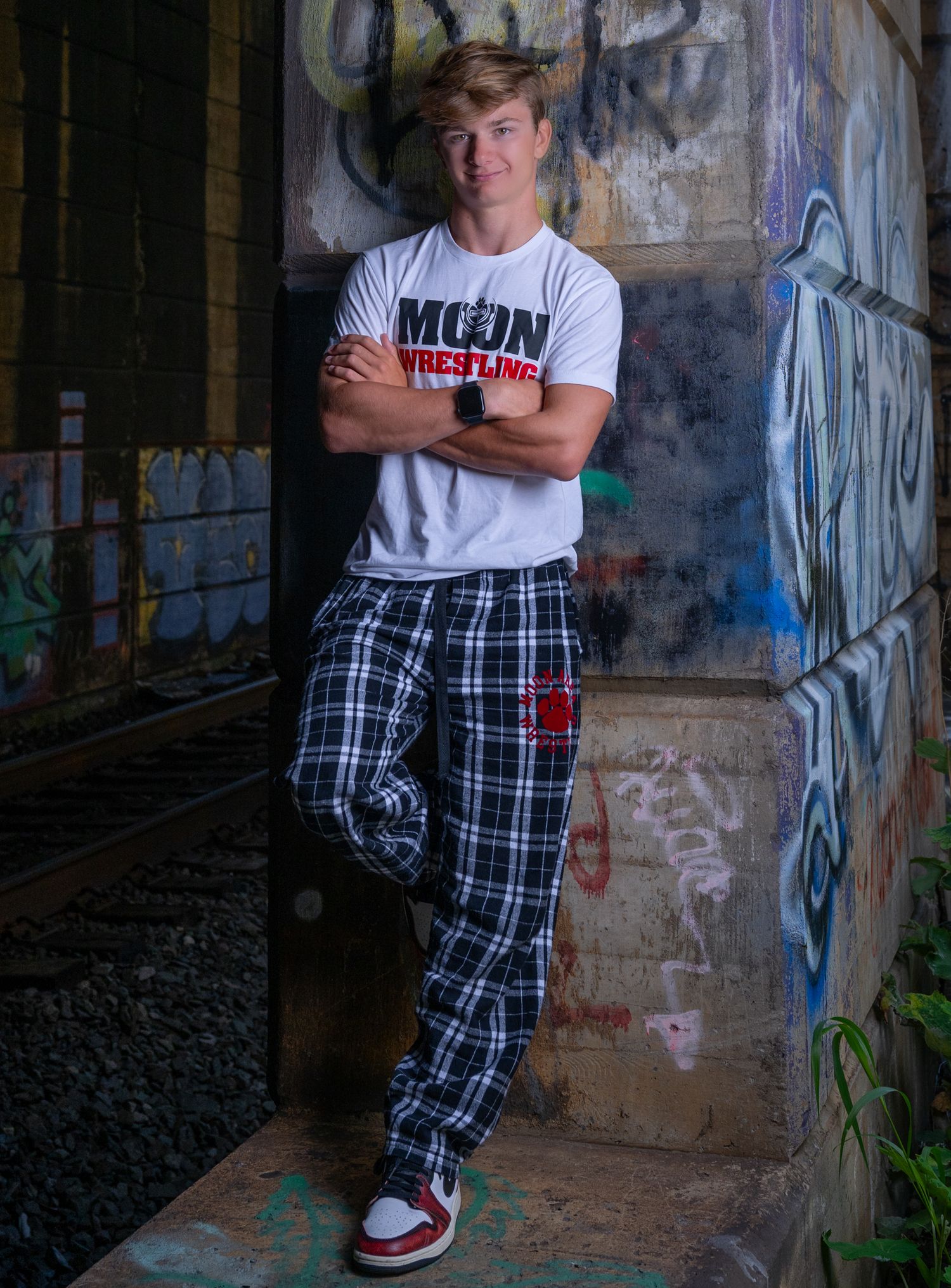 Portrait session with person in plaid pants against graffiti wall.