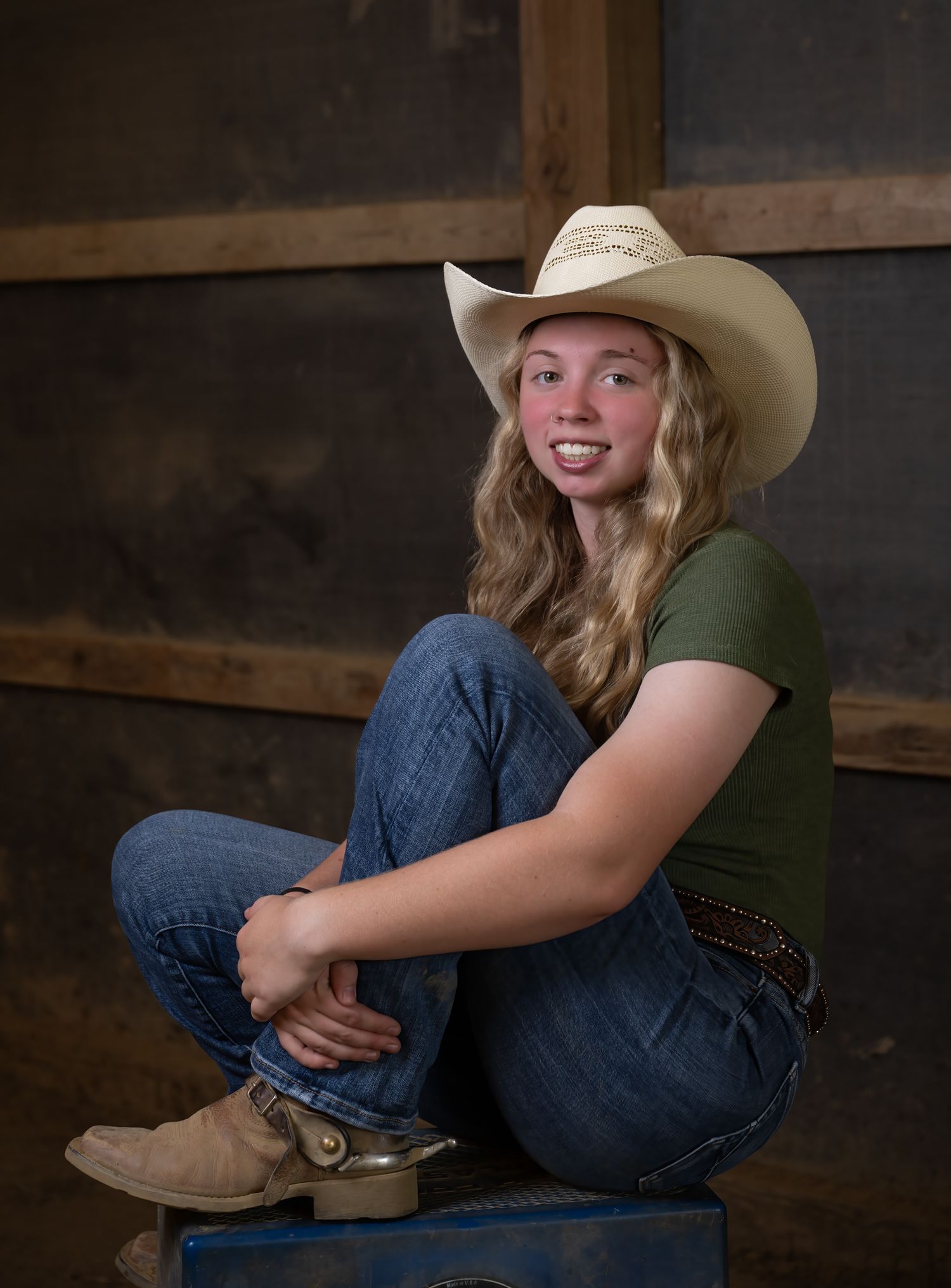 Western-style portrait with cowboy boots and hat in rustic barn setting.