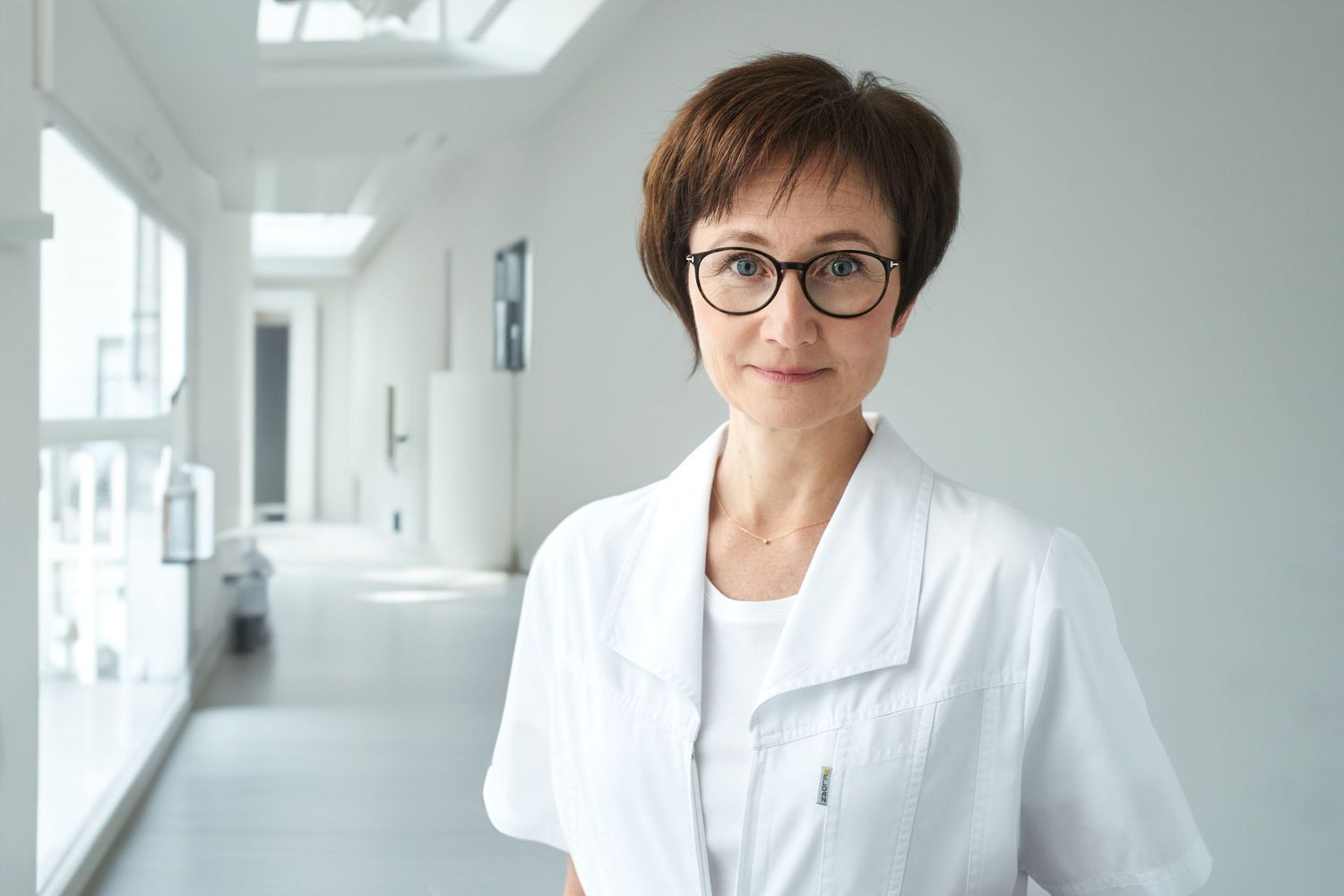 Female doctor in white coat standing in a bright modern medical hallway.