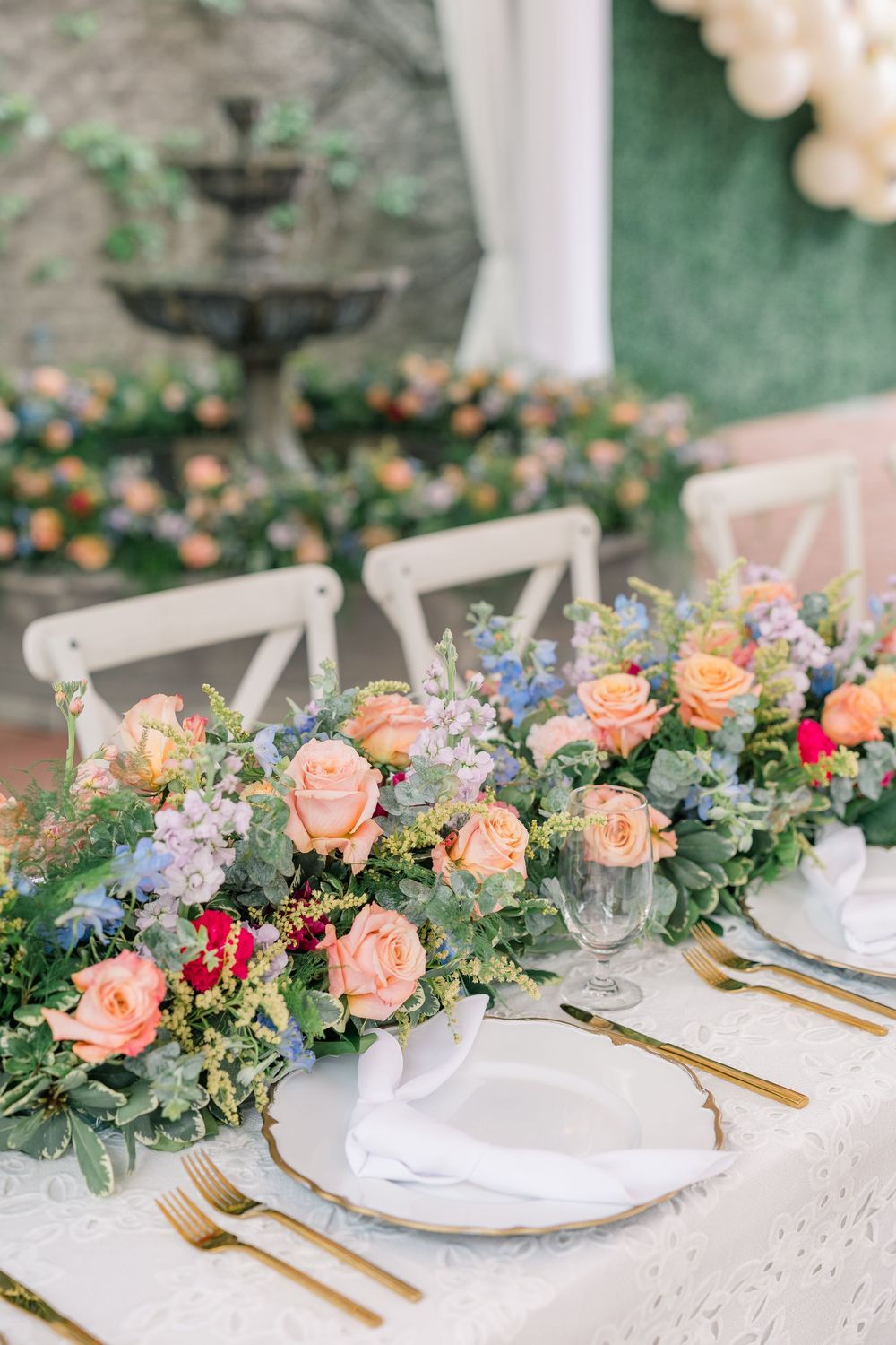 Elegant wedding table setting with peach roses and eucalyptus garland centerpiece, white plates and gold flatware.