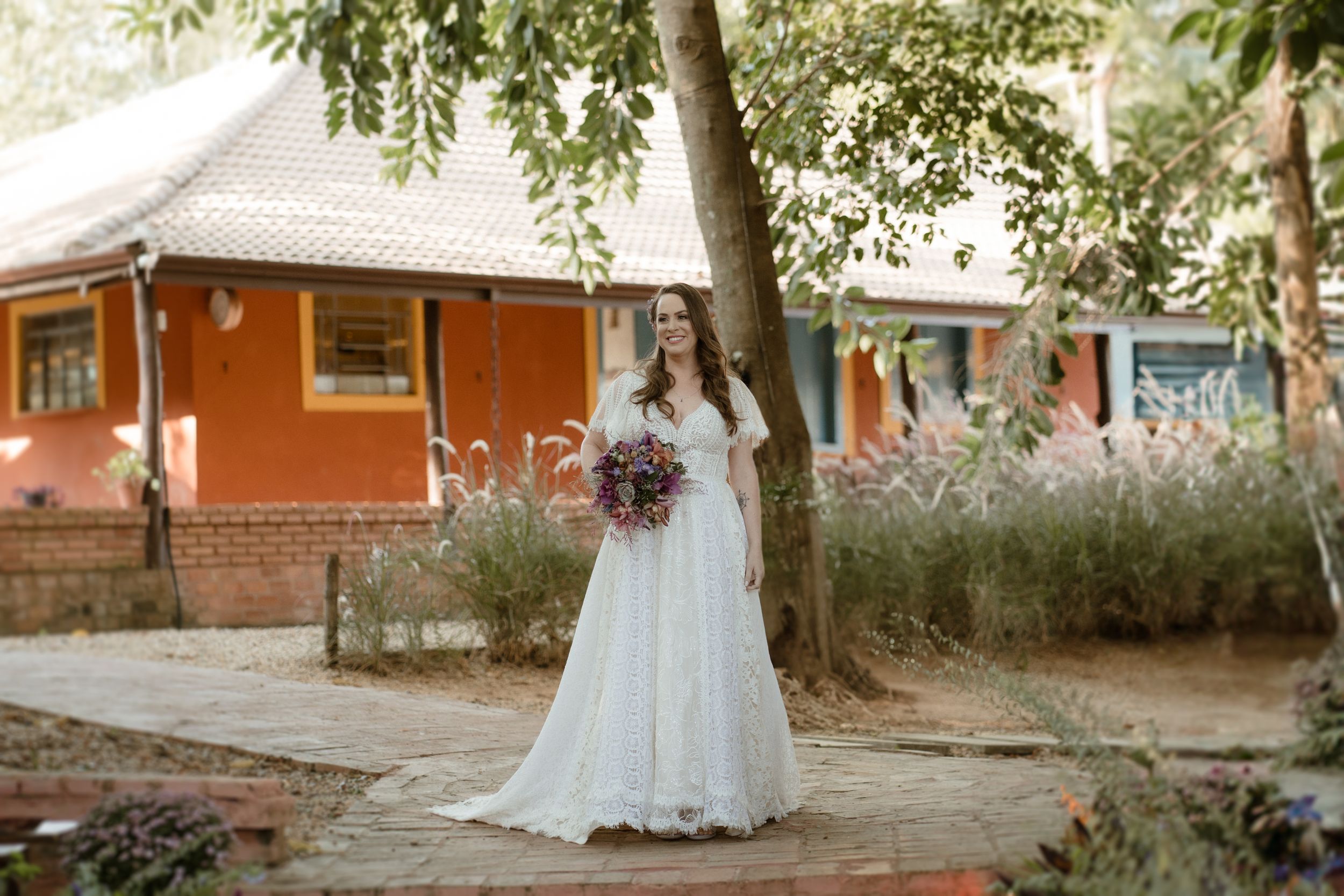 A couple in wedding attire walking together on a paved path surrounded by greenery.
