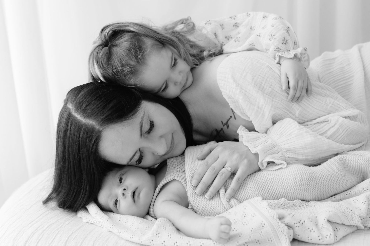 Intimate black and white portrait of family members resting together on white bedding.