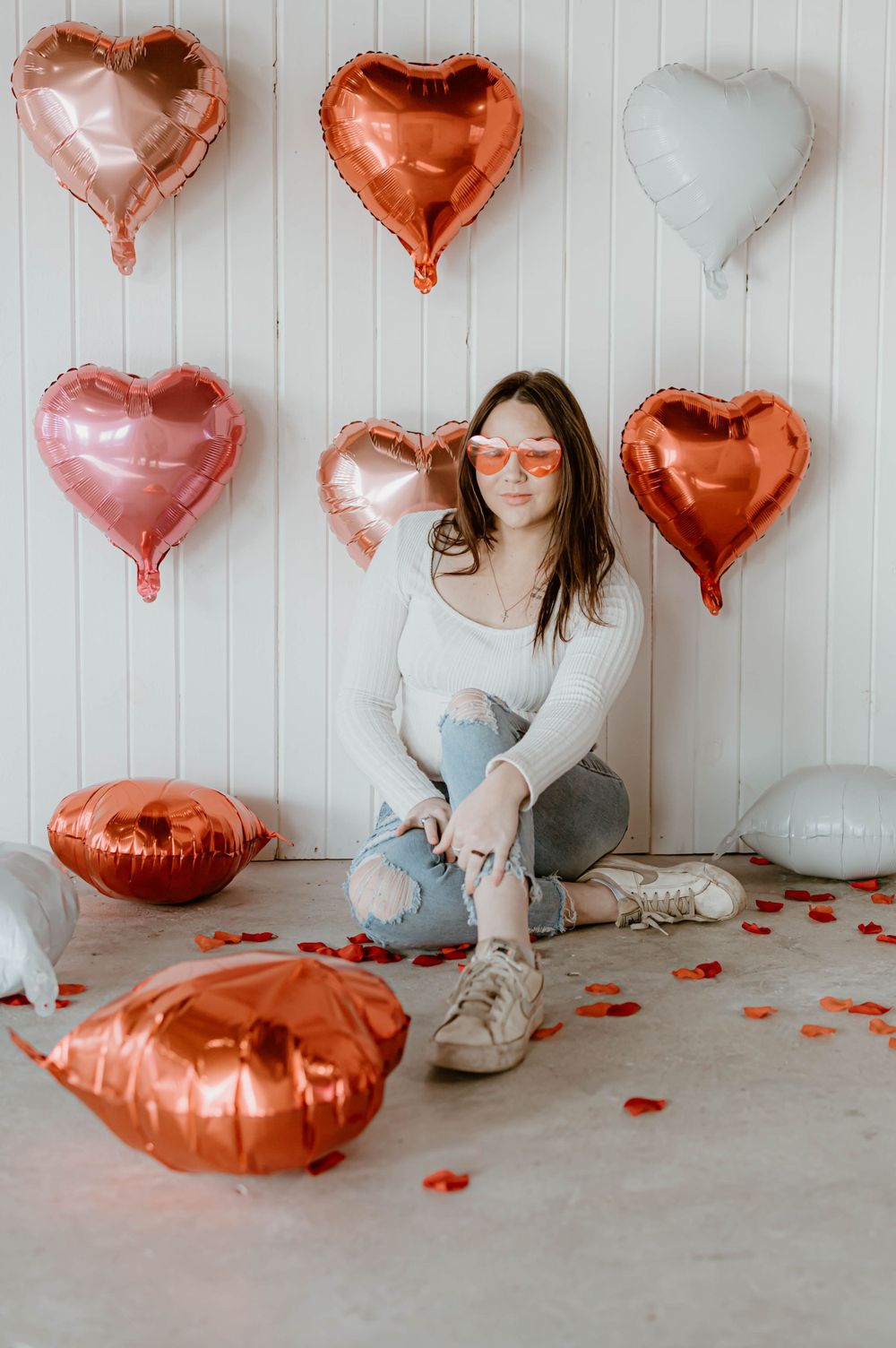 Valentine's photo setup against white wall with rose gold heart balloons, blush and white hearts scattered on floor.