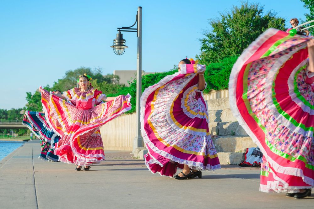 Dancers in vibrant pink and white traditional Mexican dresses perform a spinning dance routine outdoors.