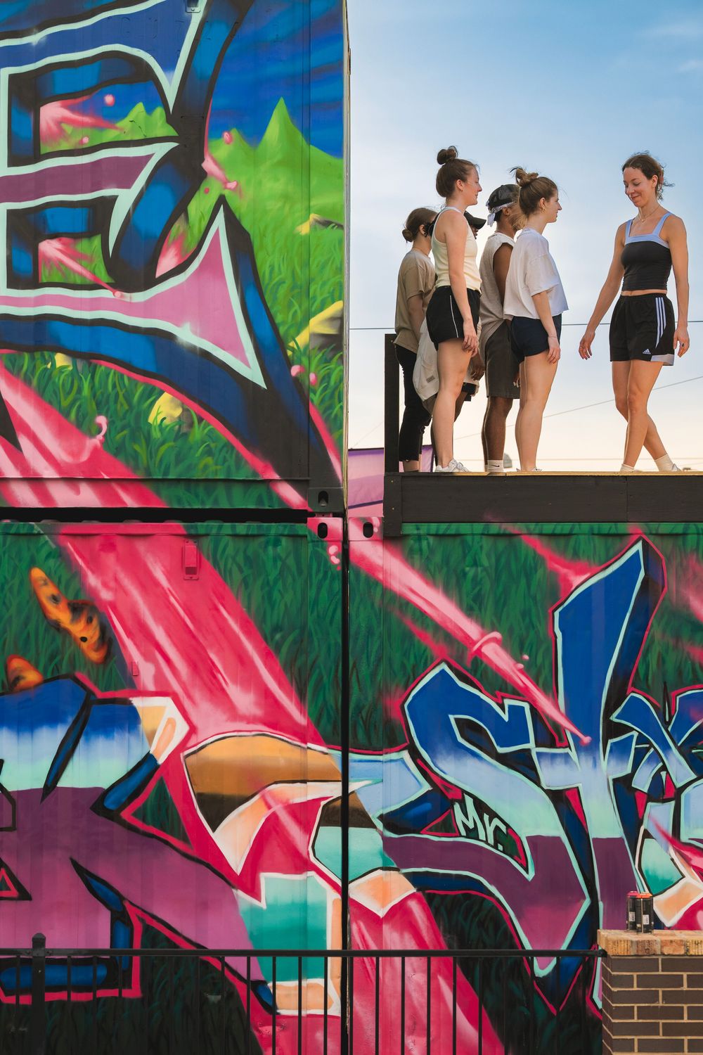 Colorful graffiti mural on a wall features vibrant pink and blue tones with people walking along the top edge.