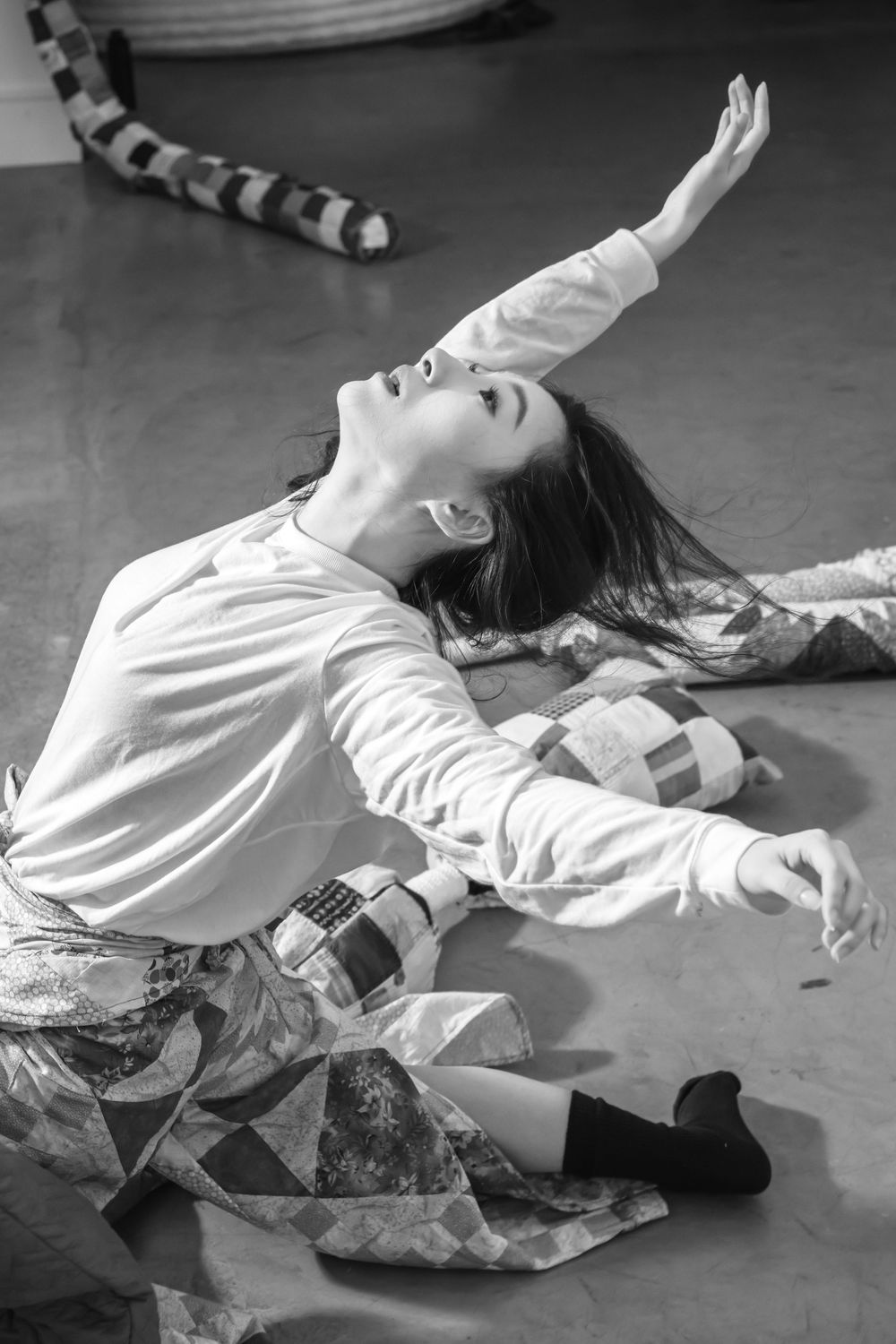 A dancer performs an expressive movement on the floor in a flowing white top and patterned skirt during a dramatic pose.
