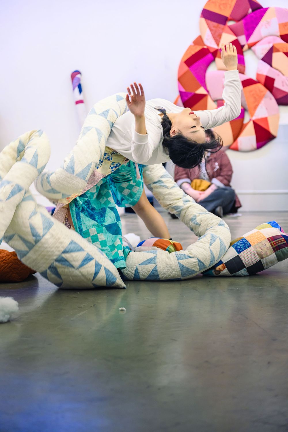 A sequence of dance movements shows a performer in a white costume rolling on a dark floor beneath pink geometric wall art.