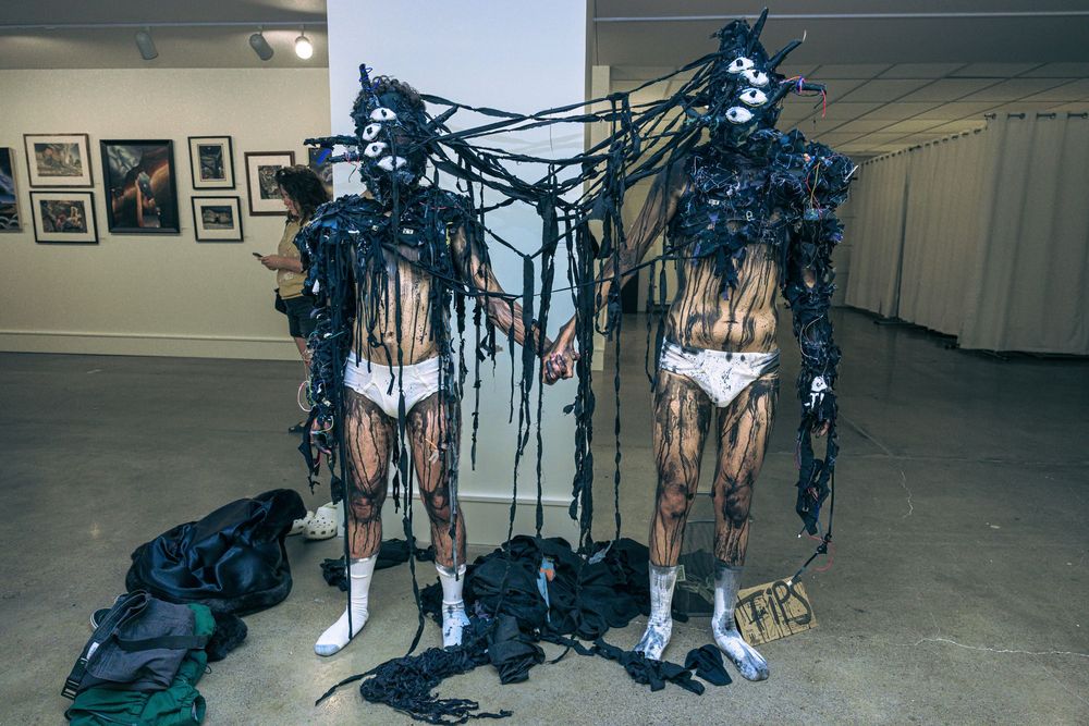 Art gallery installation features dark blue sculptural figures suspended in a white exhibition space.
