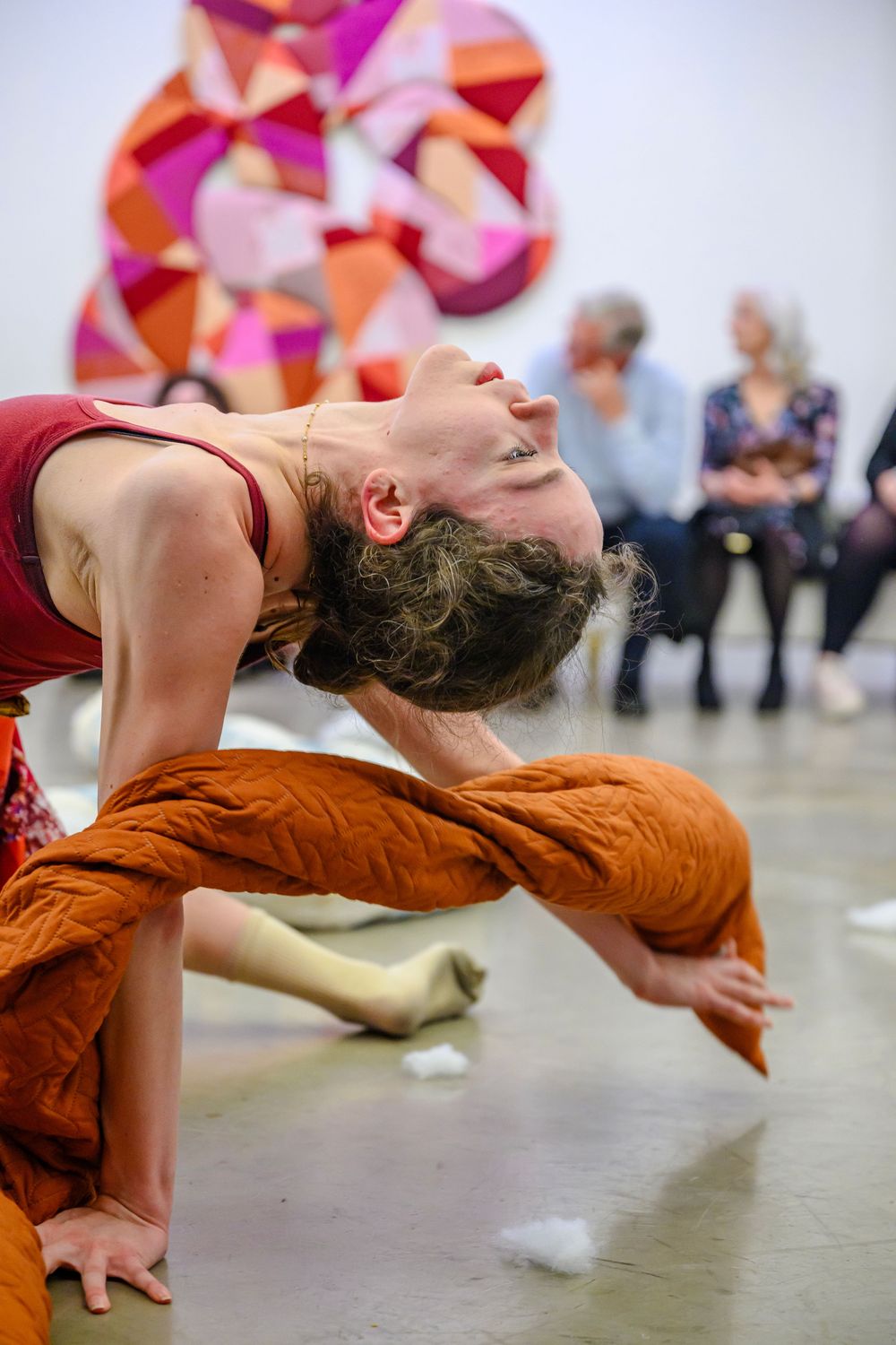A dancer in an orange outfit performs a dramatic floor movement sequence in a studio with colorful wall art.