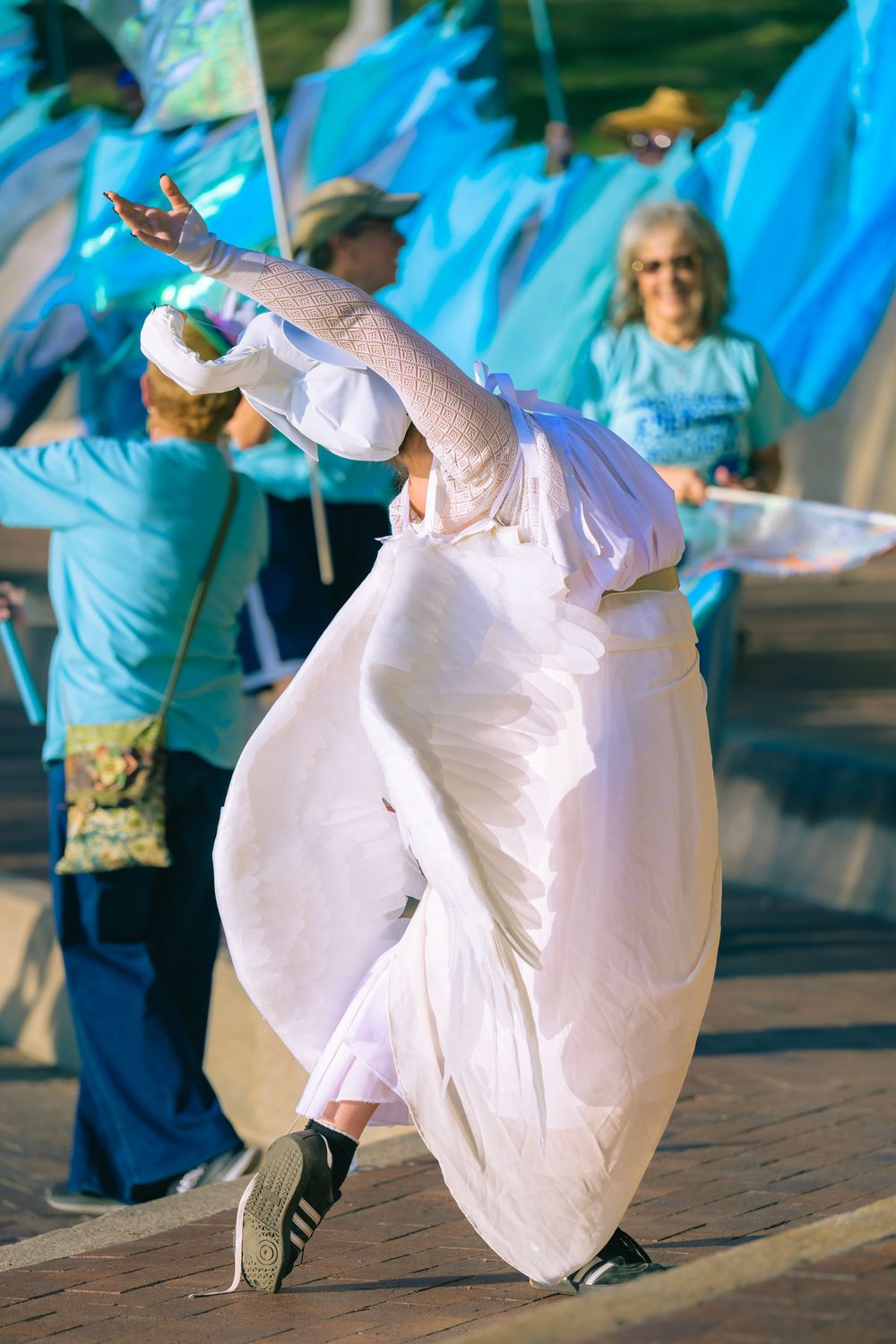 Dancers in white flowing dresses perform graceful twirling movements against a blue-lit backdrop at an outdoor event.