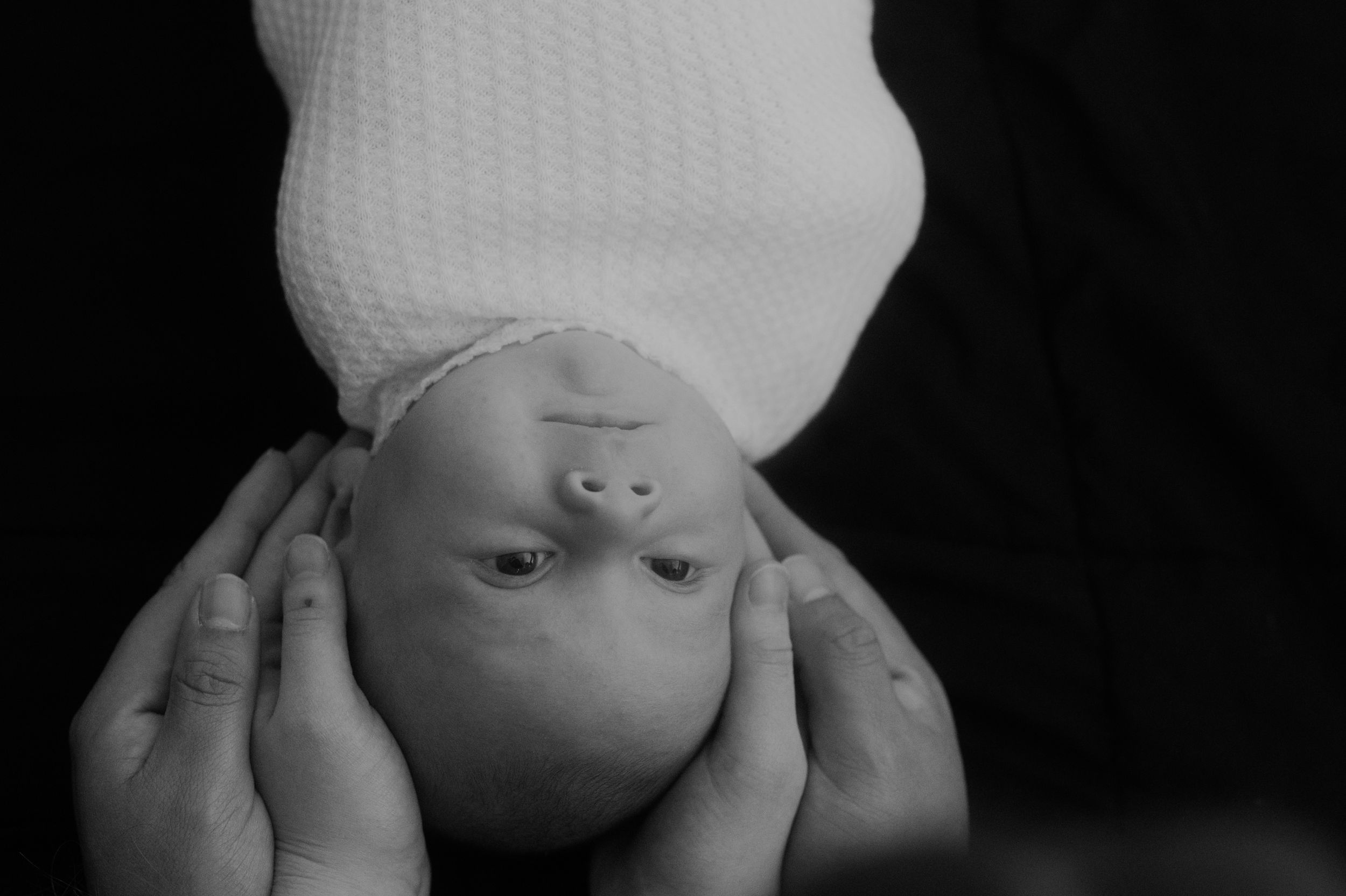 High contrast black and white image of newborn with white hat.