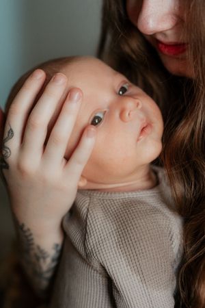 Close-up portrait of a baby being held by tattooed hands.