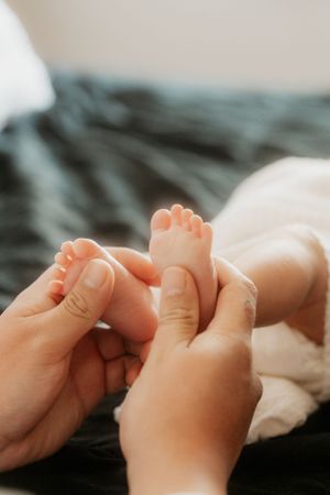 Close up of tiny baby feet being gently held by adult hands against dark fabric.