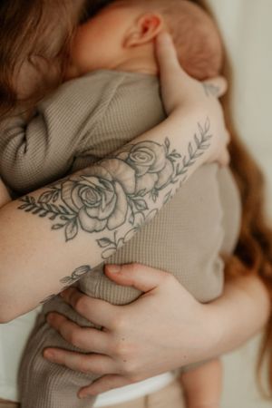 Close-up of floral tattoo on arm while holding infant in gray clothing.