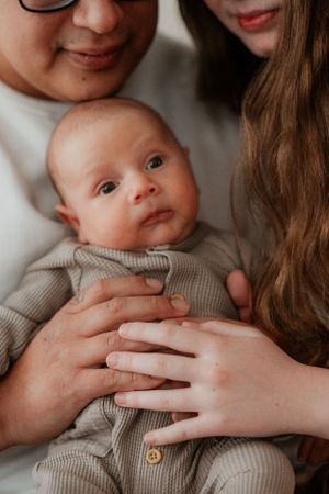 Close-up portrait of baby in gray onesie held by loving parents.