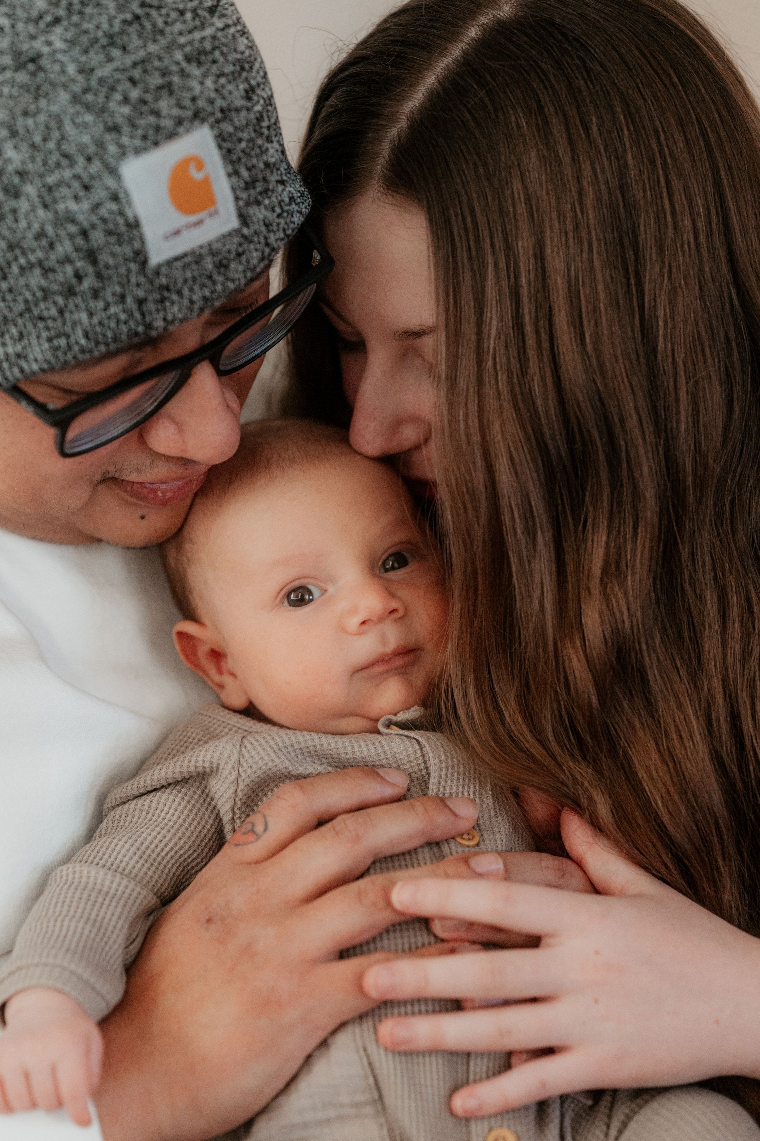 Intimate family moment with baby in gray onesie being embraced by parents.