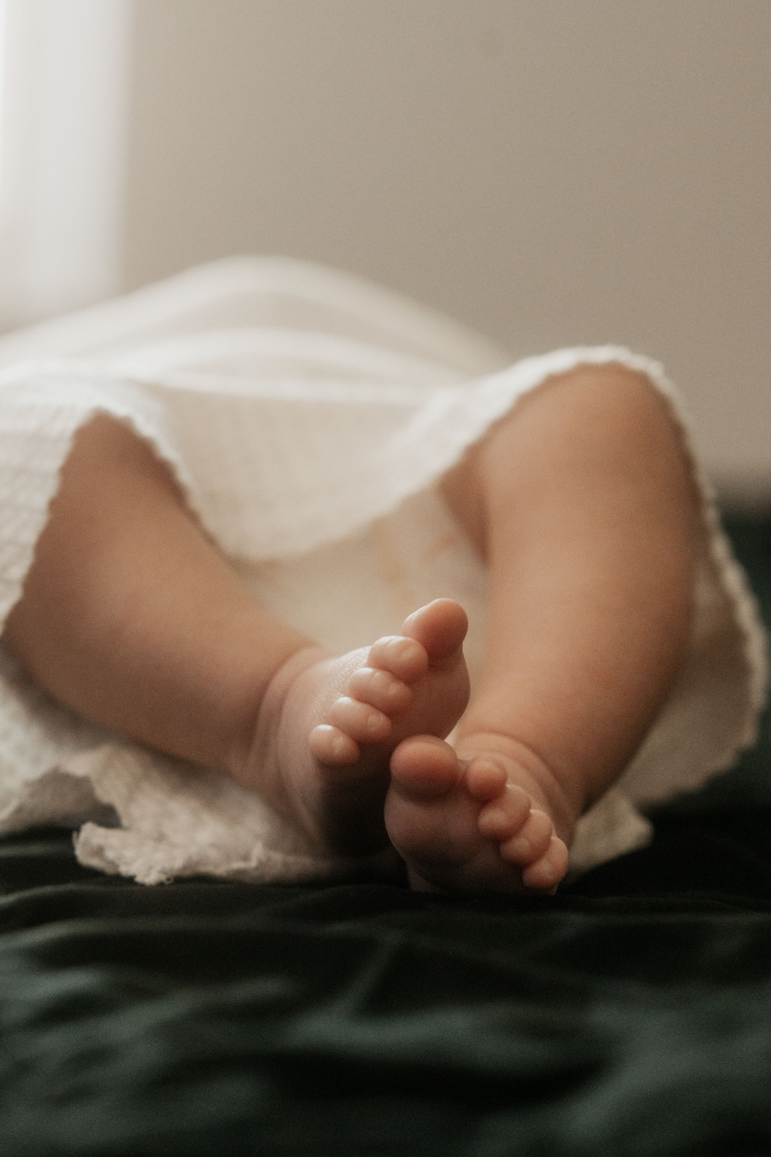 Tiny baby feet peeking out from under white blanket on black background.
