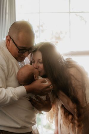 Intimate family moment as parents share affection with their newborn baby by window light.