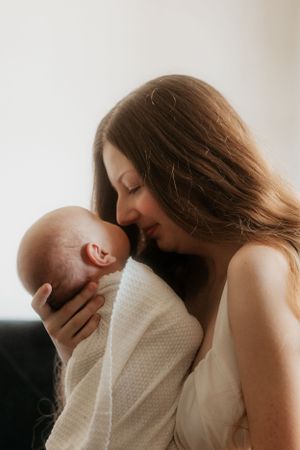 Mother with flowing hair embraces newborn lovingly by window.