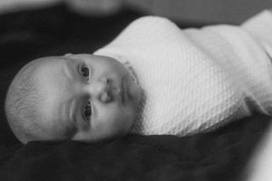 Black and white portrait of an infant wrapped in a textured white blanket.