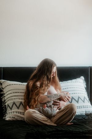 Woman with long hair sits on dark couch with infant in casual home setting.