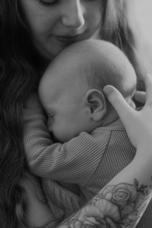 A black and white image showing tender moment between a tattooed parent and sleeping baby.