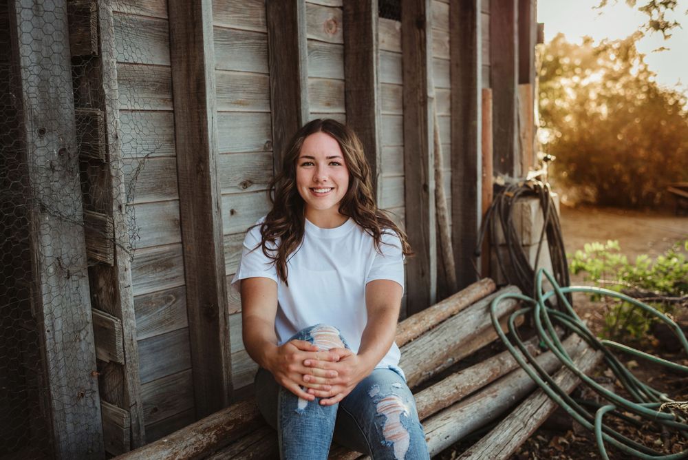 Casual portrait sitting on wooden steps outside a rustic barn at sunset.