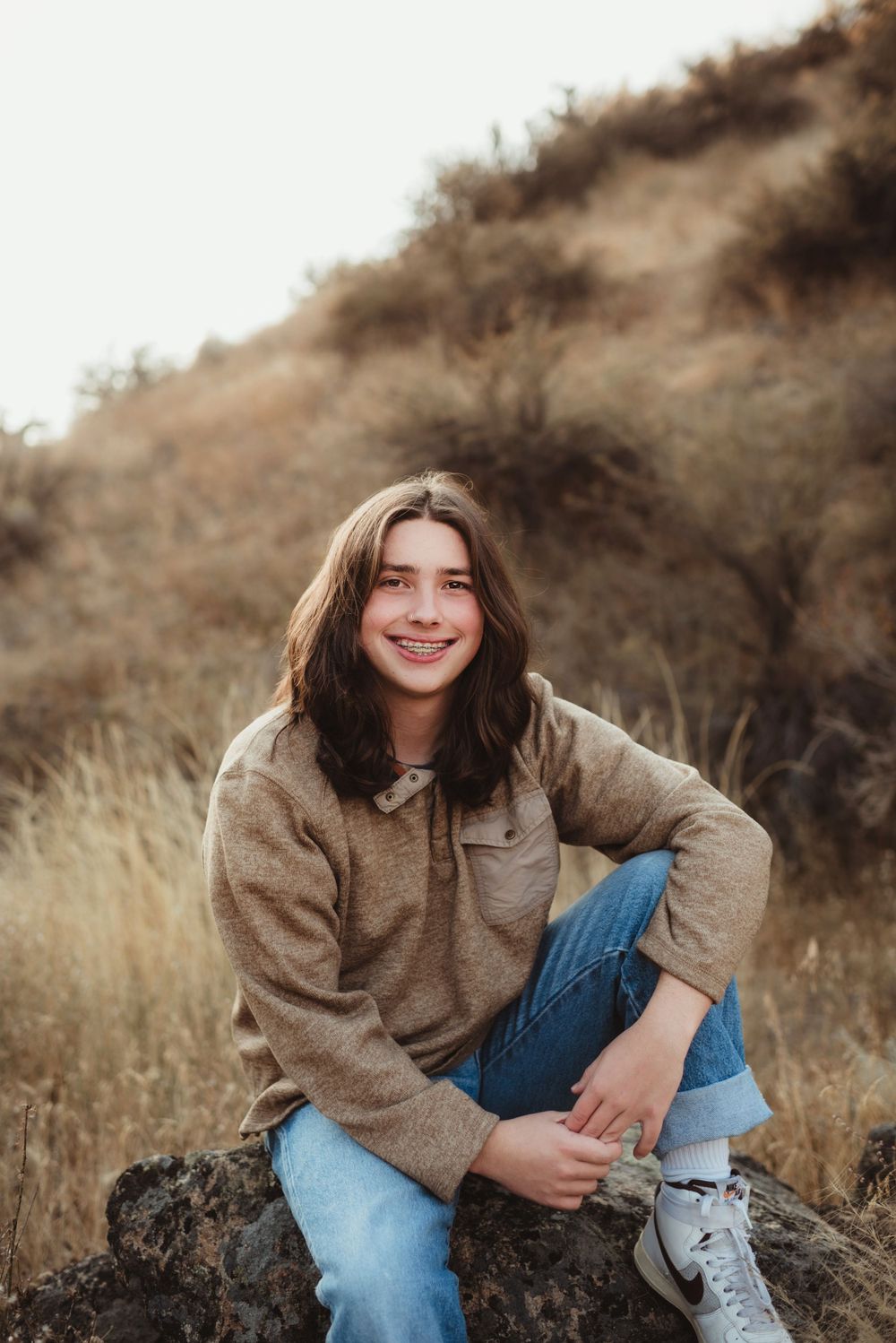 Casual portrait on a rocky outcrop wearing brown sweater and jeans in autumn setting.
