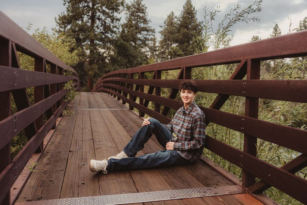 Someone sits casually on a wooden footbridge surrounded by trees during golden hour lighting.