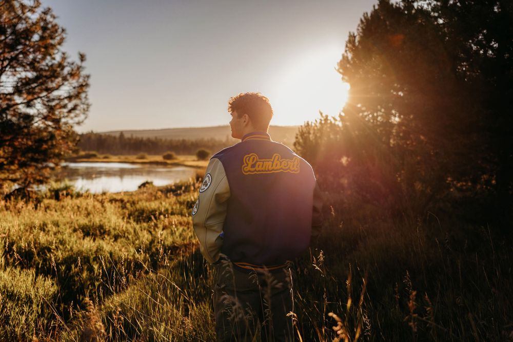 Person sits on grassy hill overlooking scenic lake at golden sunset with lens flare.