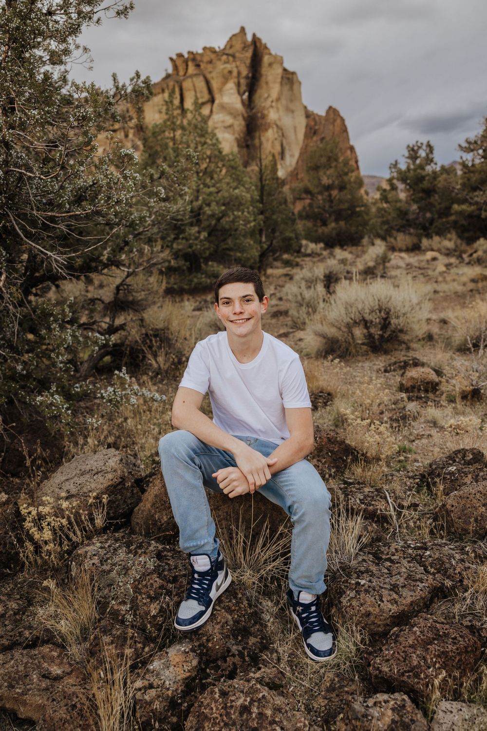 Person sitting on rock with desert cliffs and sage brush in background.