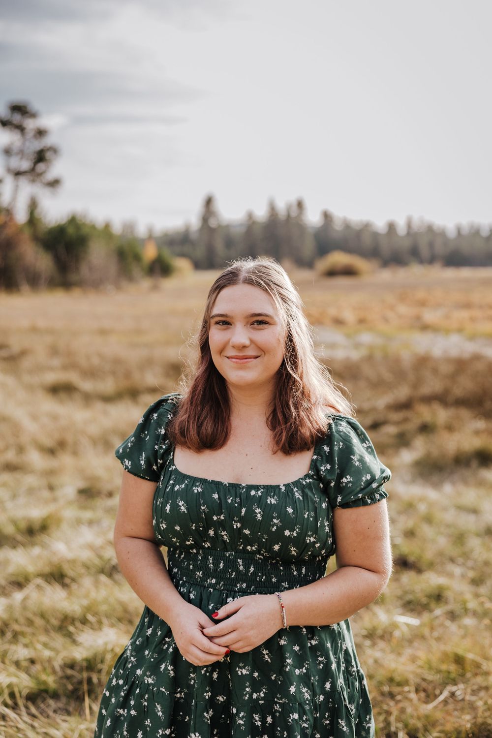 Portrait in green floral dress standing in golden autumn field.