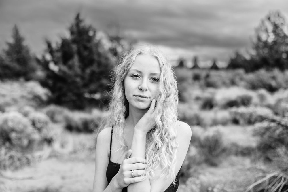 Black and white portrait against a moody desert landscape with evergreen trees.