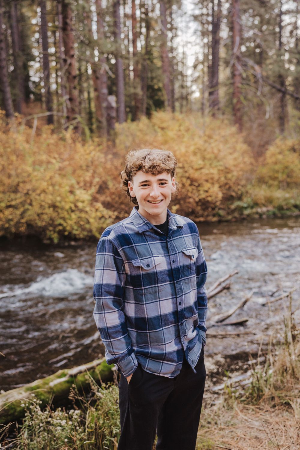 A casual portrait by a flowing river in a wooded autumn setting.