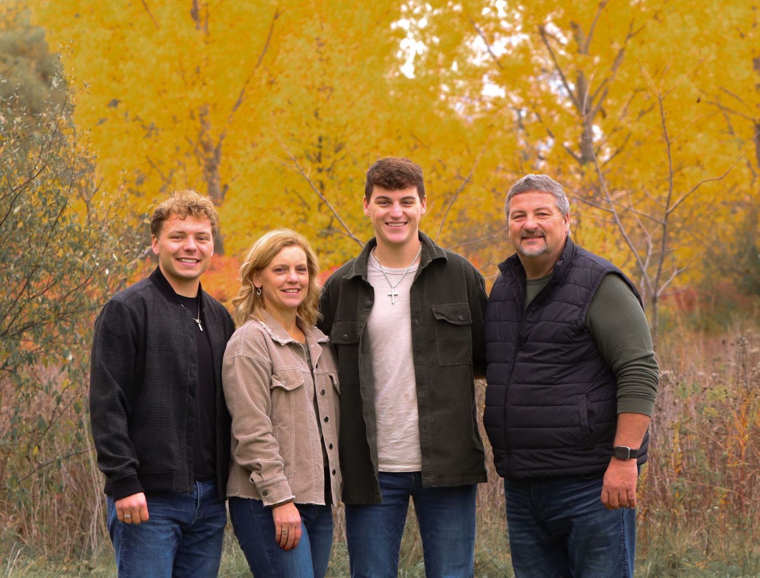 Outdoor family portrait with autumn foliage featuring four people against golden yellow trees.