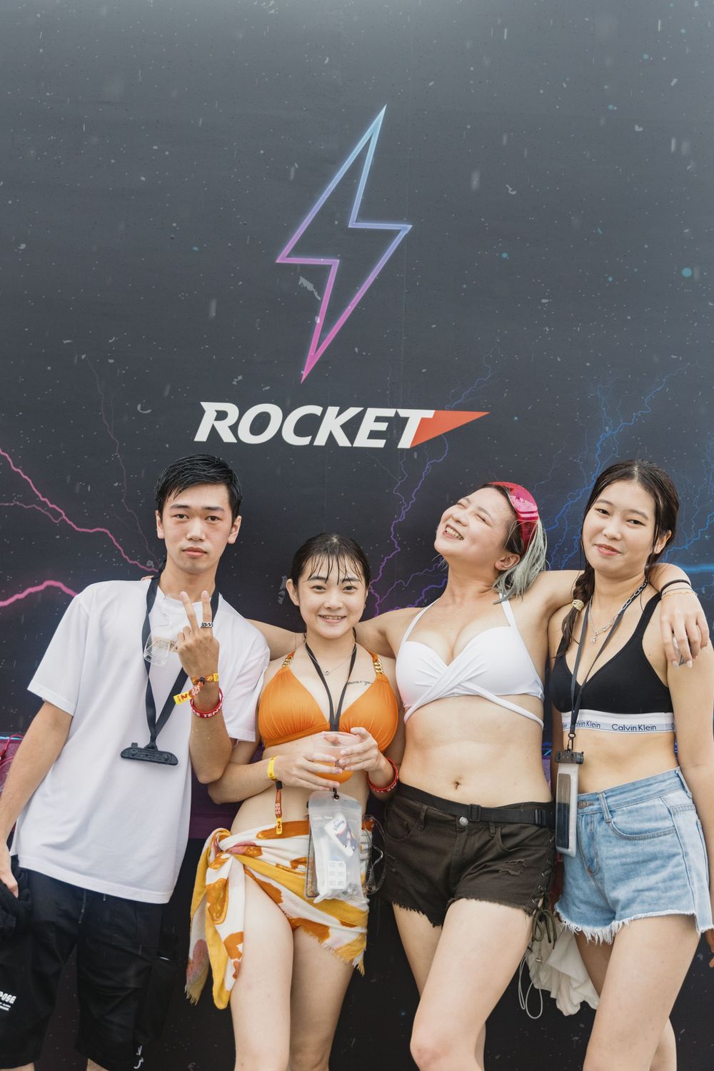 Four young friends posing together in front of Rocket brand backdrop at music festival.