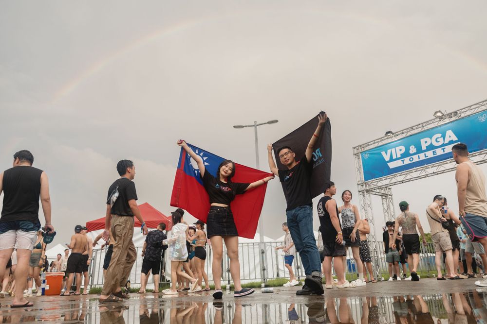 Festival crowd holds Taiwan and Australian flags under a rainbow at an outdoor music event.
