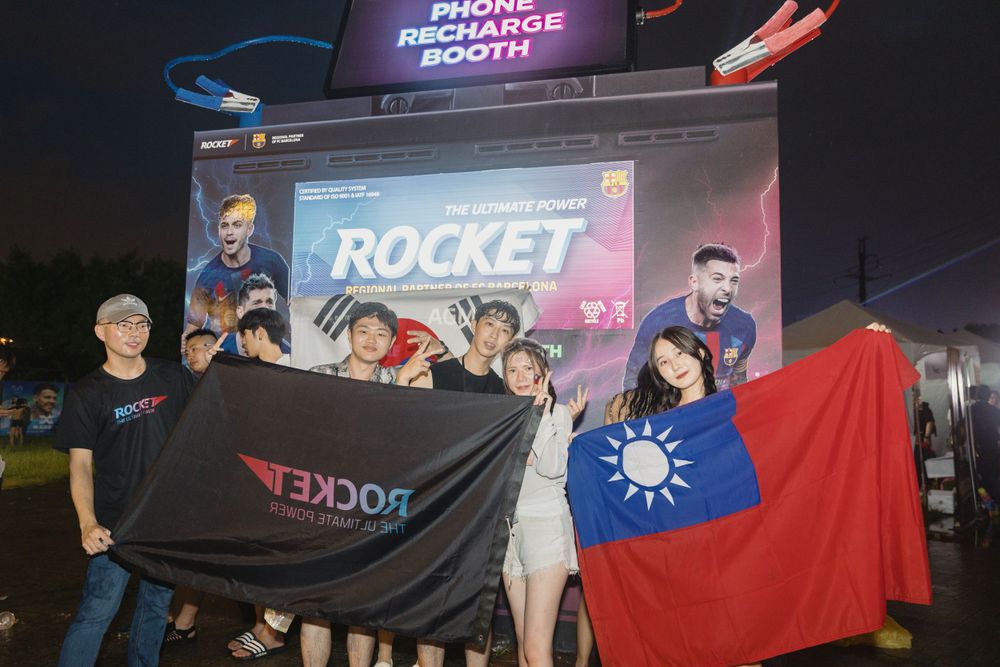 Group of fans holding Rocket brand flag and Taiwan flag at a Phone Recharge Booth.