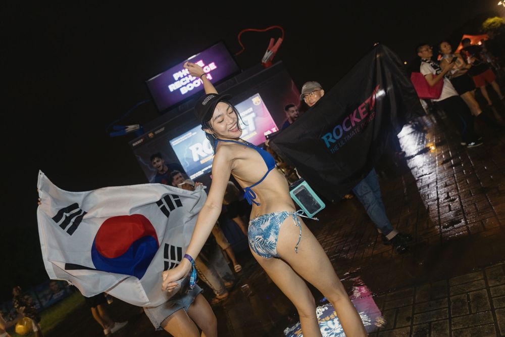 Woman in festival attire holds South Korean flag at an outdoor nighttime music event.